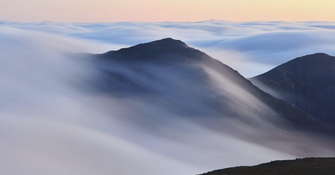 L'immagine raffigura un paesaggio con montagne e nebbia