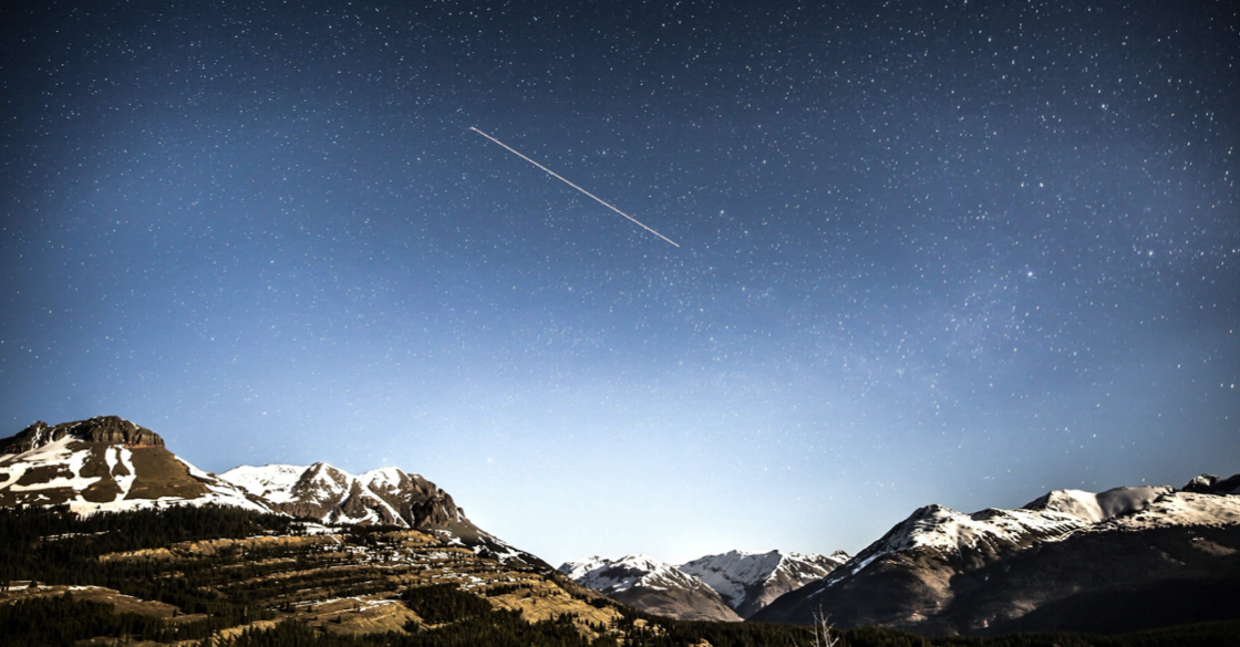 Immagine con delle montagne innevate e un cielo stellato