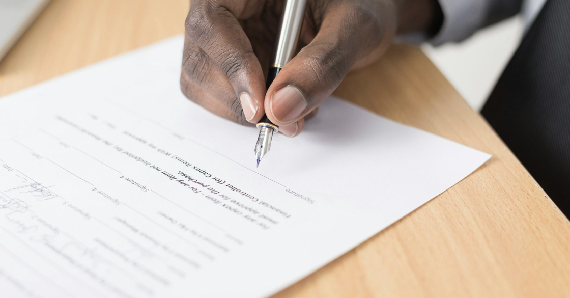 L'immagine raffigura la mano di un uomo con una penna, intento a firmare un documento